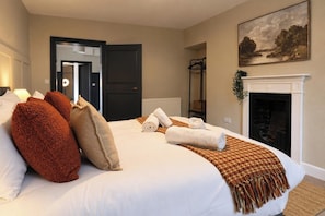 A hotel room with a bed, a fireplace, a painting, and a door leading to another room.