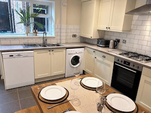 A modern kitchen with white cabinetry, a dishwasher, a washing machine, a stove, and a dining area set for two with a table and chairs.