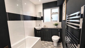 Ein modernes Badezimmer mit Badewanne, Toilette, Waschbecken und einem Fenster über dem Waschbecken.