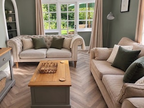 A living room with a beige sofa, a wooden coffee table, and a herringbone-patterned floor.