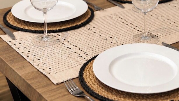 Een eettafel gedekt met witte borden, heldere wijnglazen en zwarte onderzetters.
