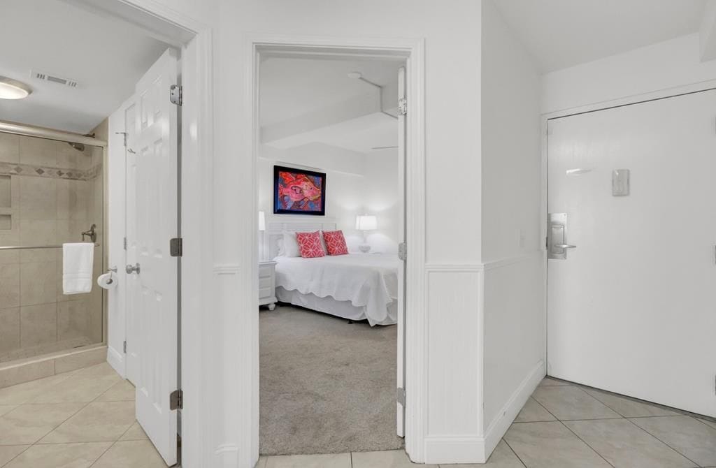 A hotel room with a shower, a bed with a white bedspread and red pillows, a flat-screen TV mounted on the wall, and a white door.