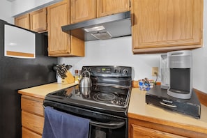A compact kitchen with wooden cabinets, a black stove, a kettle, and a Keurig coffee maker. - Remodeled  1-bedroom condo with garage in Anchorage perfect for a relaxing stay (Anchorage)