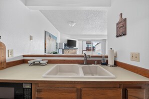 Una cocina con un lavaplatos doble, armarios de madera, lavavajillas y una encimera con una botella de jabón para lavar platos.