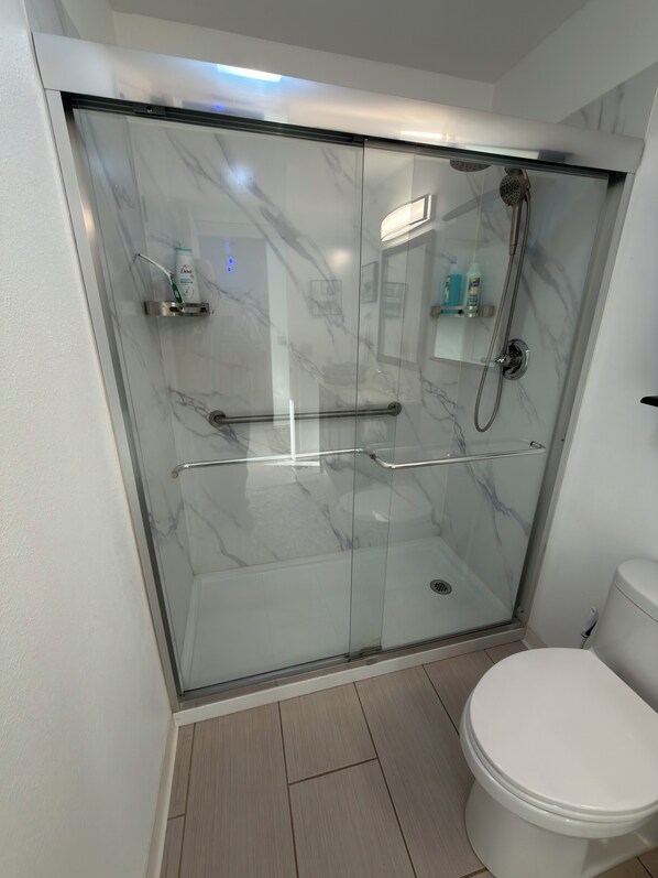 A modern bathroom with a glass-enclosed shower, a white toilet, and a marble backsplash.