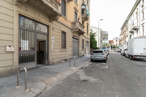 Eine Straße mit parkenden Autos und Gebäuden mit vergitterten Fenstern und heruntergelassenen Rollläden.