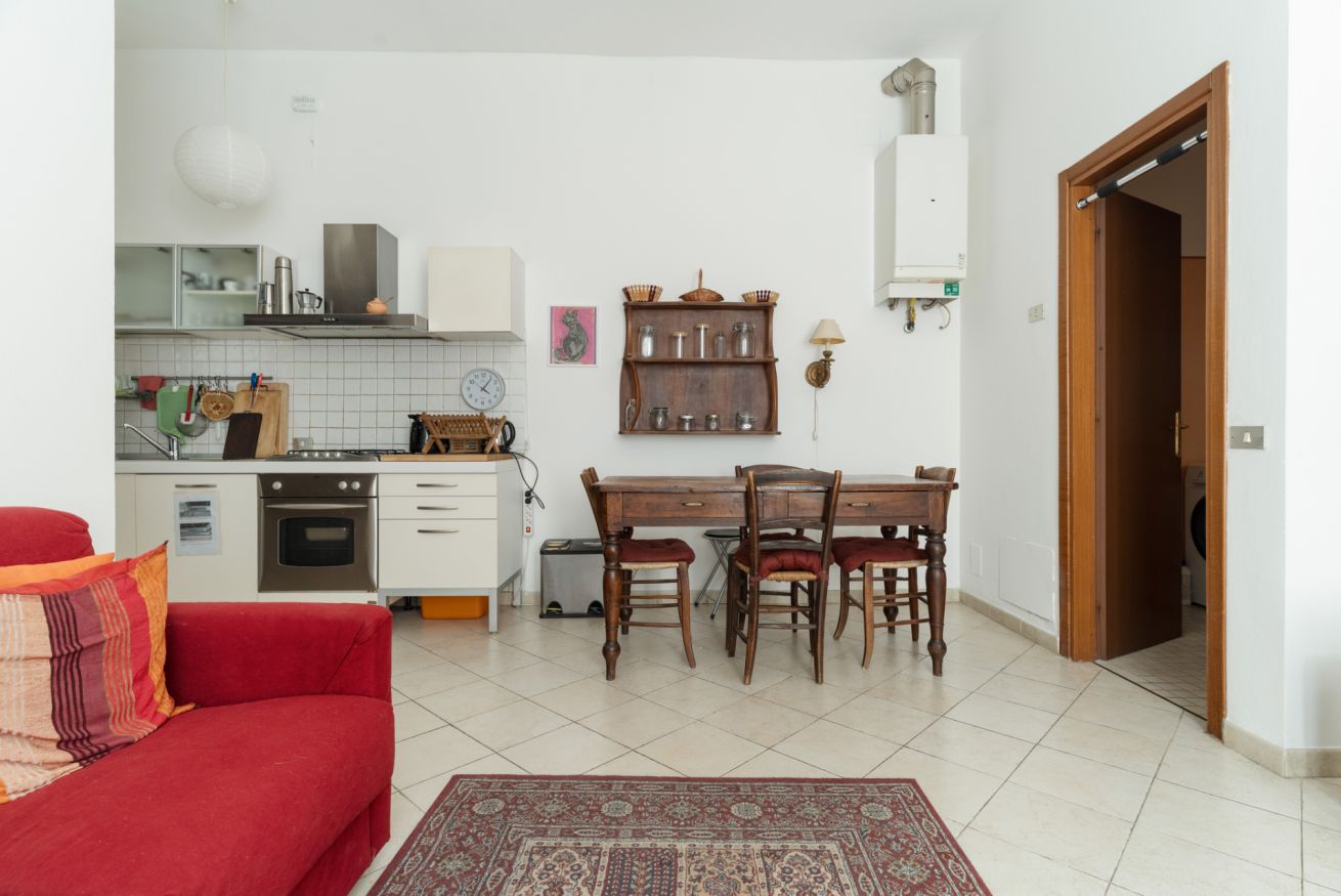 A compact living space with a kitchenette, a dining area with a wooden table and chairs, a red sofa, and a patterned rug.