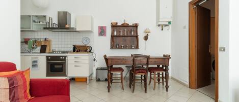 A compact living space with a kitchenette, a dining area with a wooden table and chairs, a red sofa, and a patterned rug.