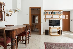 Ein Essbereich mit Holztisch und Stühlen, einem Fernseher auf einem Holzschrank und einem Bücherregal mit Büchern.