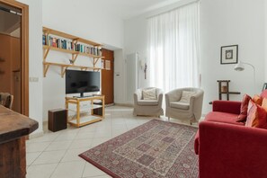 A living room with a television, two armchairs, a red sofa, a patterned rug, and a bookshelf. - A comfortable and bright 64 square meters apartment, perfect for four people, located on the first floor of a building with an elevator (NOT accessible to people with disabilities).The property is in a highly strategic location for exploring the city, si (Milan)