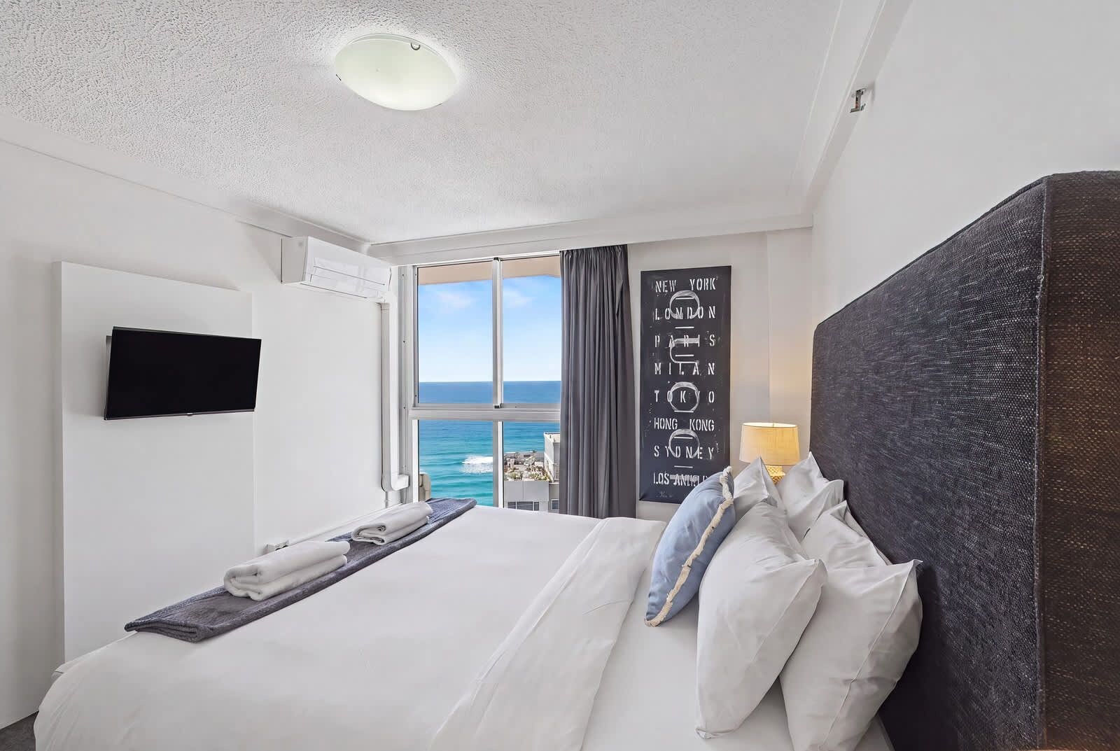 Habitación de hotel con cama, televisor de pantalla plana, ventana con vista panorámica de la ciudad y una obra de arte colgada en la pared.