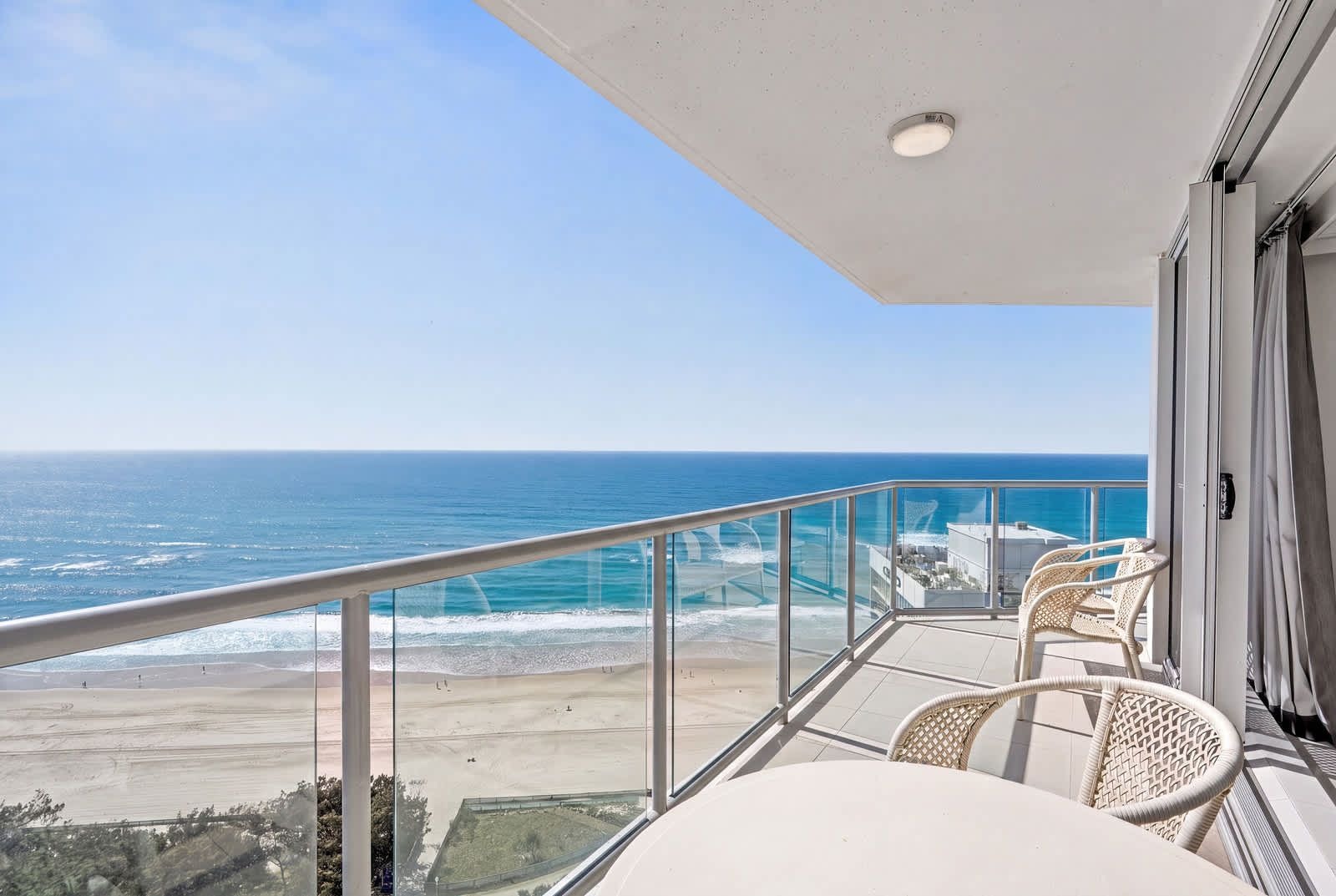 A balcony with a view of the ocean, a glass railing, and two wicker chairs.