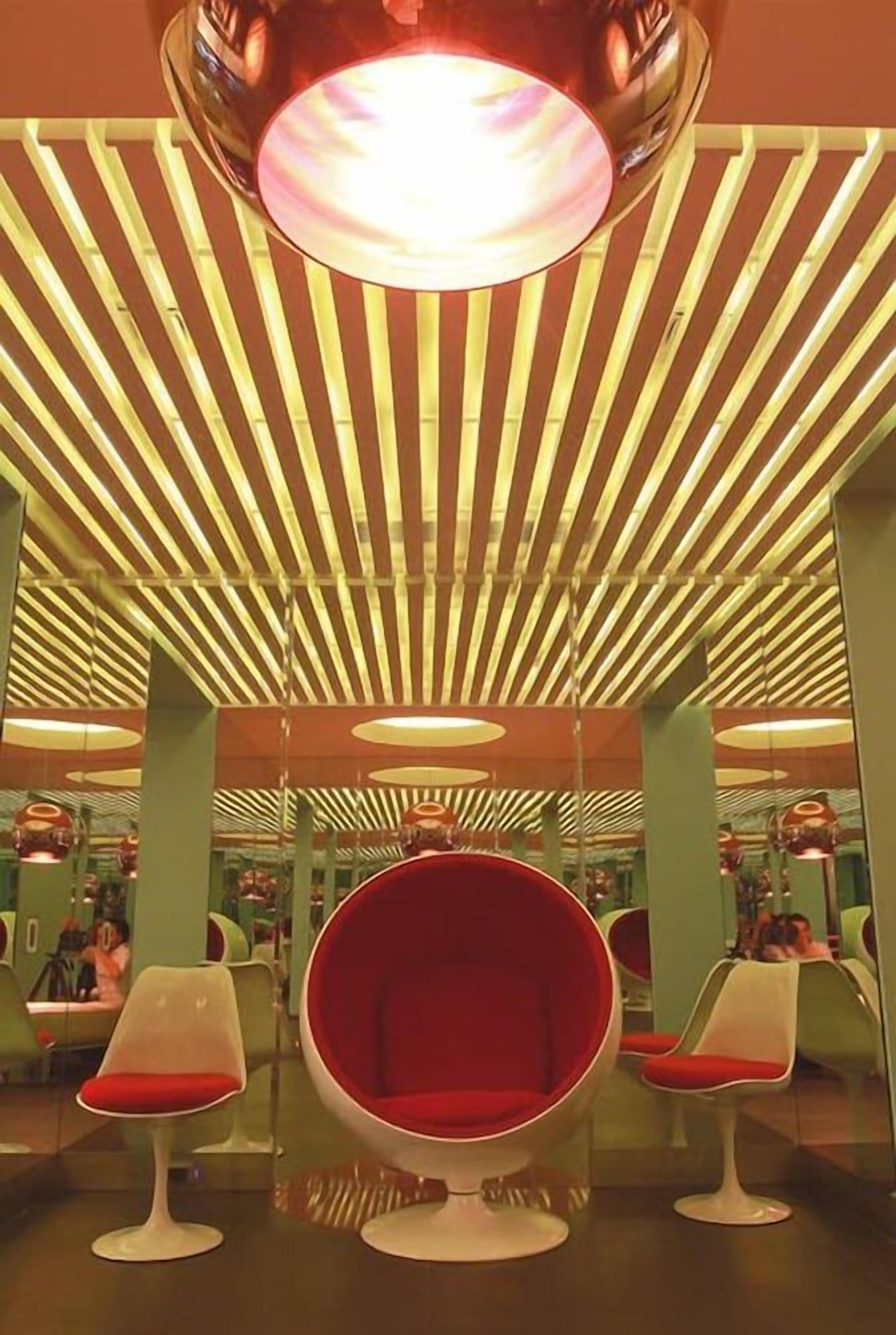 Un interior moderno con un techo que presenta luminarias lineales y una silla roja central.