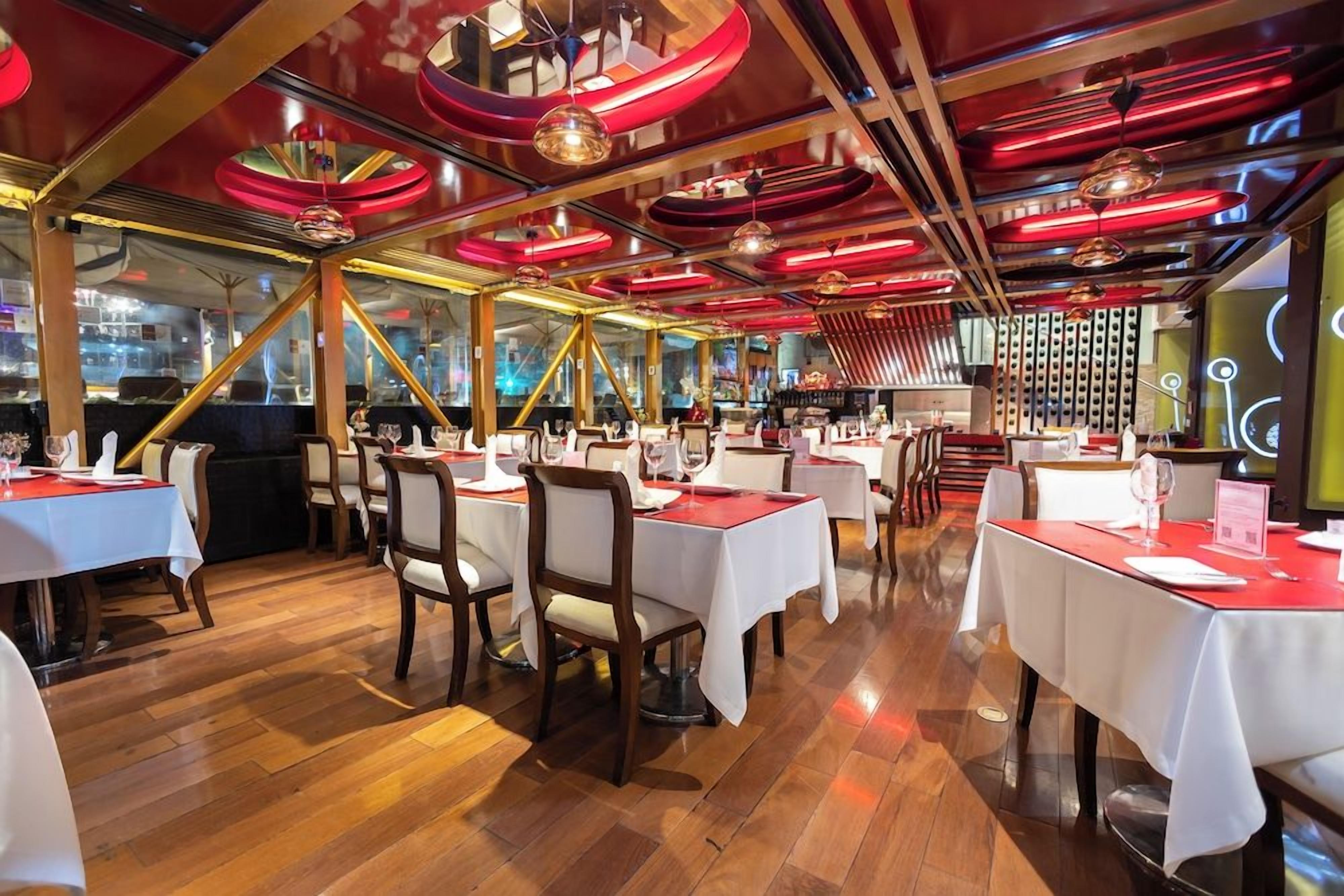 Interior de restaurante con mesas dispuestas para comer, pisos de madera y un diseño de techo moderno.