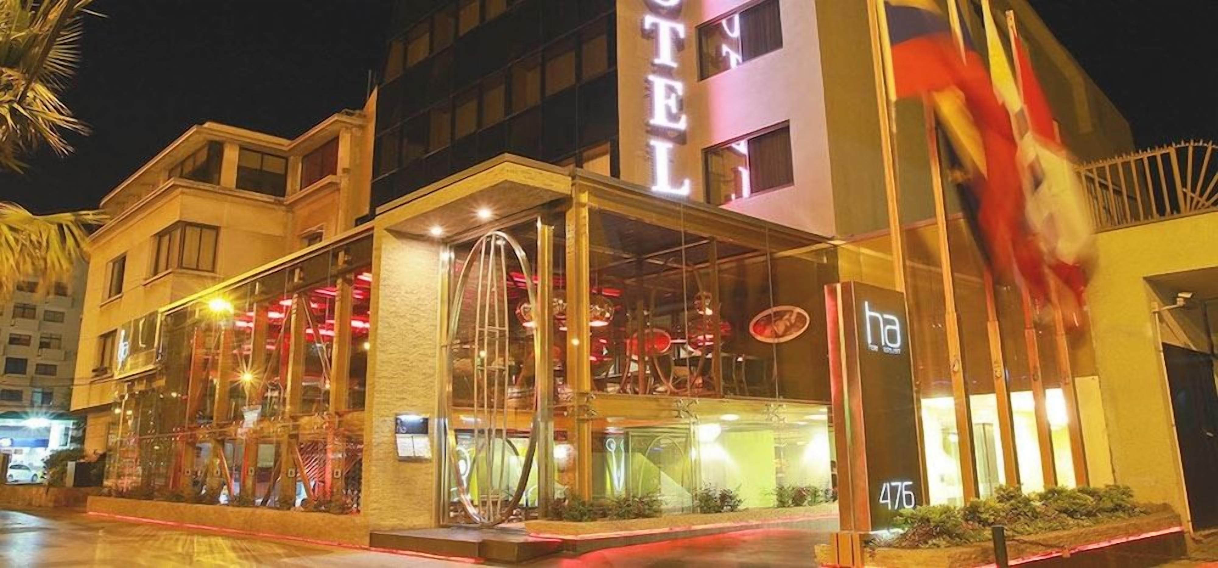 Un hotel con fachada de vidrio, una entrada visible y una bandera en el exterior.