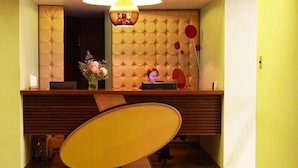 A hotel reception area with a tufted wall, a reception desk, a chair, and a vase with flowers. - Hotel Ankara (Vina del Mar)