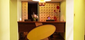 A hotel reception area with a tufted wall, a reception desk, a chair, and a vase with flowers. - Hotel Ankara (Vina del Mar)