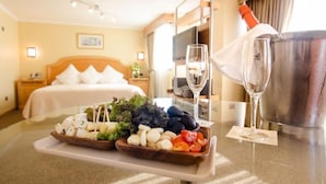 A hotel room with a bed, a bedside table with a bottle of champagne, a tray with cheese and vegetables, and two glasses of champagne. - Hotel Ankara (Vina del Mar)