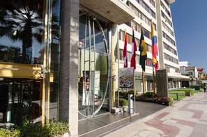 Un hotel moderno con amplios ventanales de vidrio, múltiples banderas y un área exterior bien cuidada.