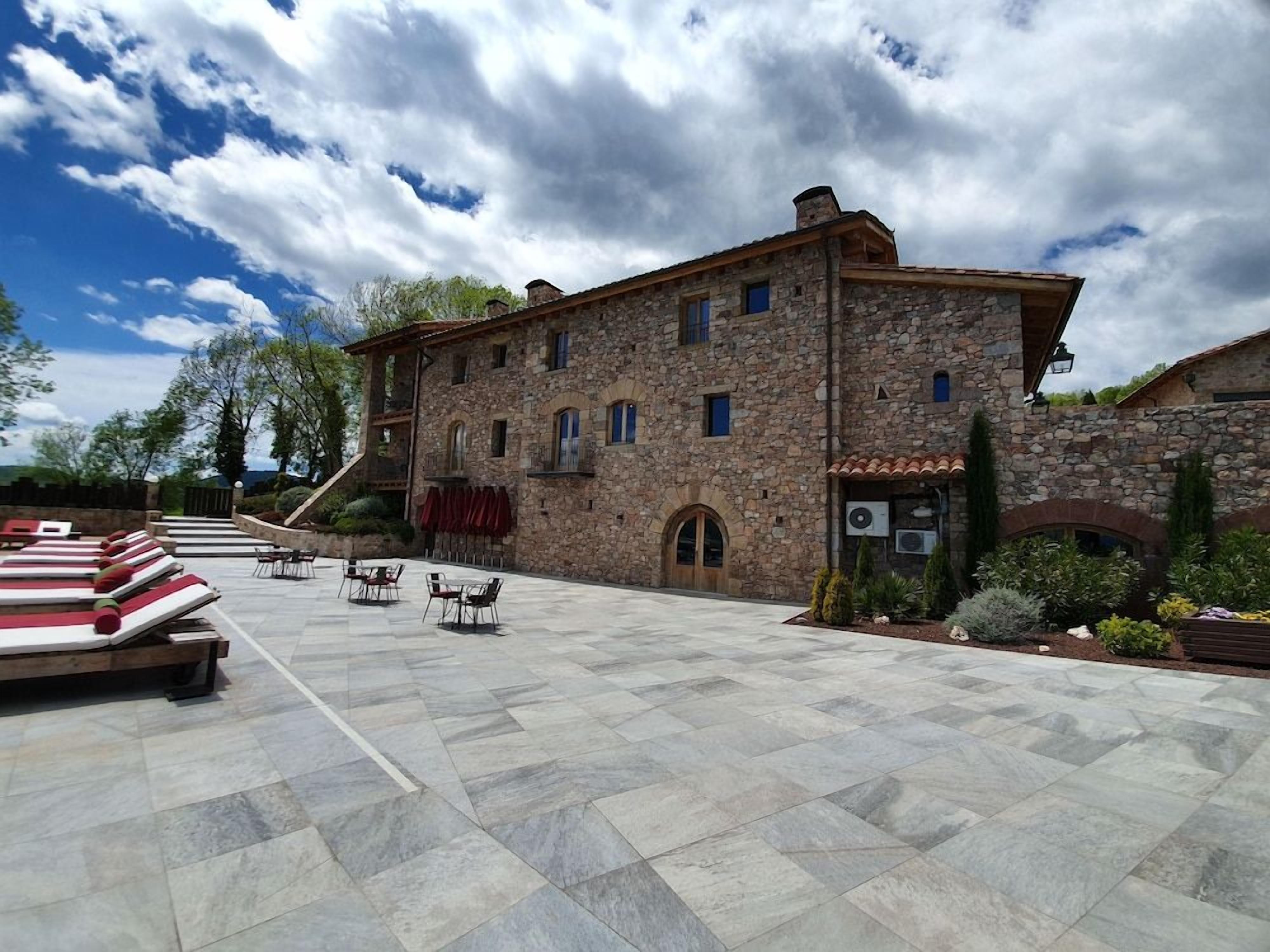 Un edificio de piedra con patio, asientos exteriores y una escalera que lleva a la entrada.