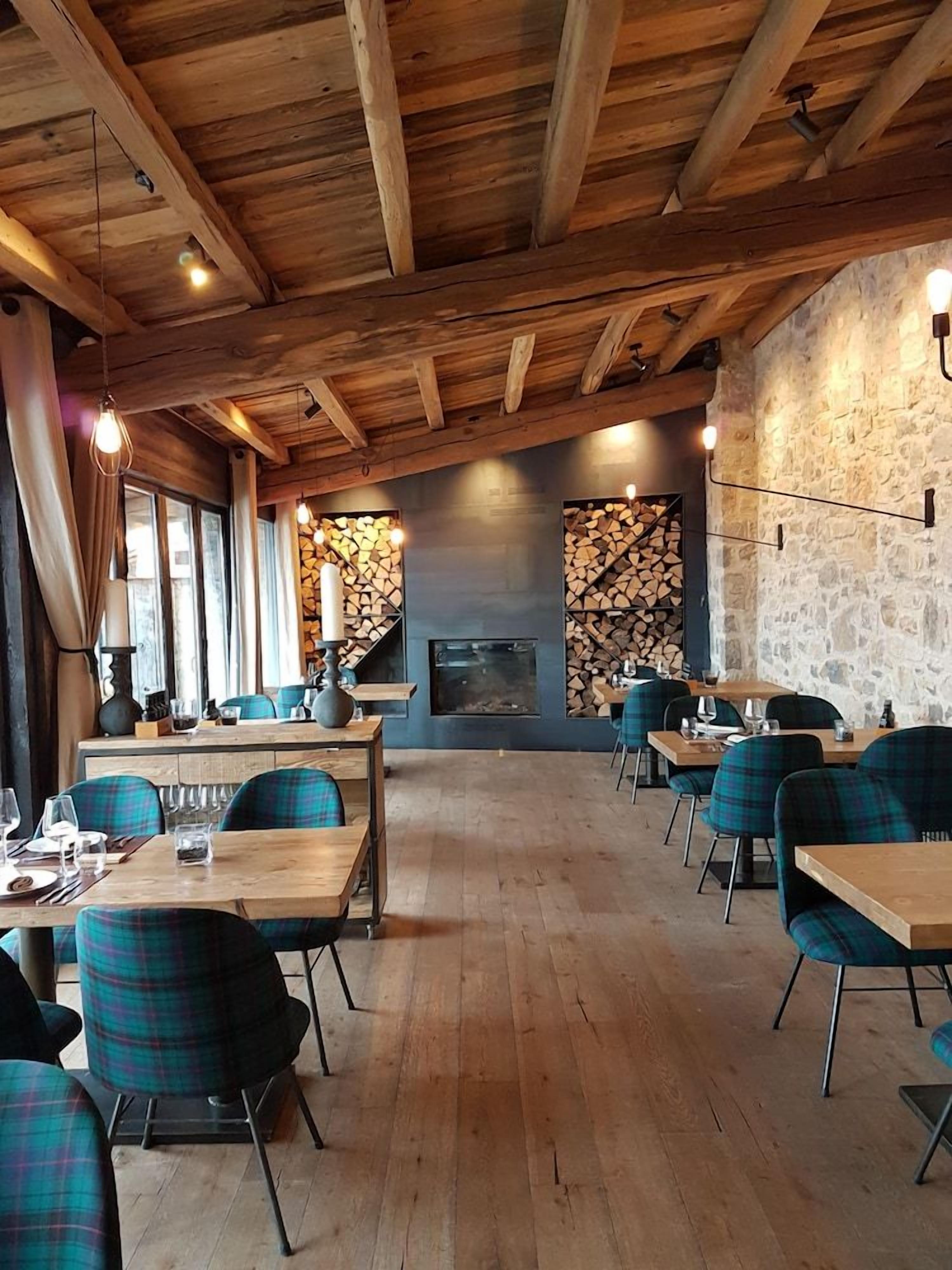 Un restaurante con vigas de madera, paredes de piedra y sillas a cuadros. Las mesas están dispuestas con vasos y cubiertos.