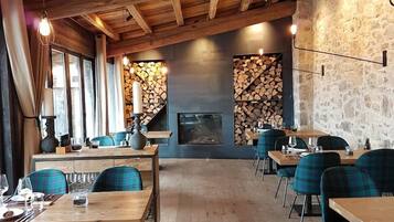 Un restaurante con vigas de madera, paredes de piedra y sillas a cuadros. Las mesas están dispuestas con vasos y cubiertos.