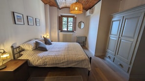 Une chambre à coucher comprenant un lit, une table de chevet, une lampe, une armoire, une fenêtre et un miroir fixé au mur.