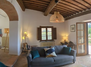 Un salon chaleureux avec un canapé, un luminaire suspendu, une fenêtre avec des volets et un radiateur.