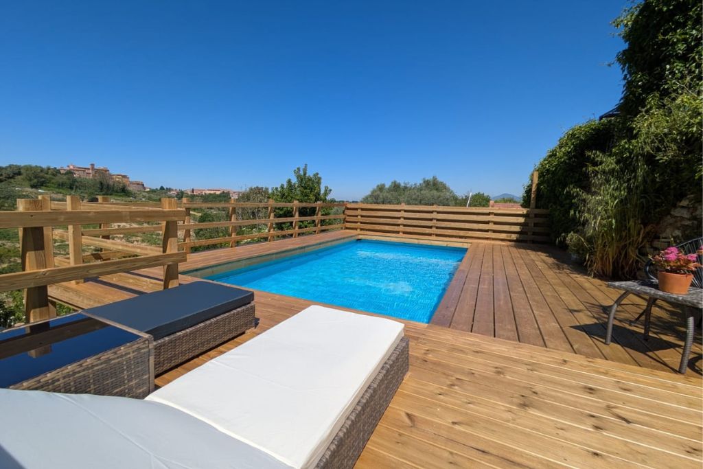 Une terrasse en bois avec une piscine, des chaises longues et une vue sur le paysage environnant.