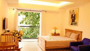 Quarto de hotel com cama, poltrona, mesa, luminária e um pôster na parede.
