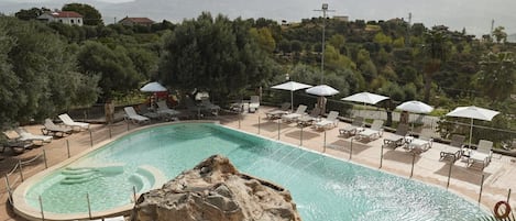 A swimming pool with lounge chairs and umbrellas, surrounded by trees and hills.