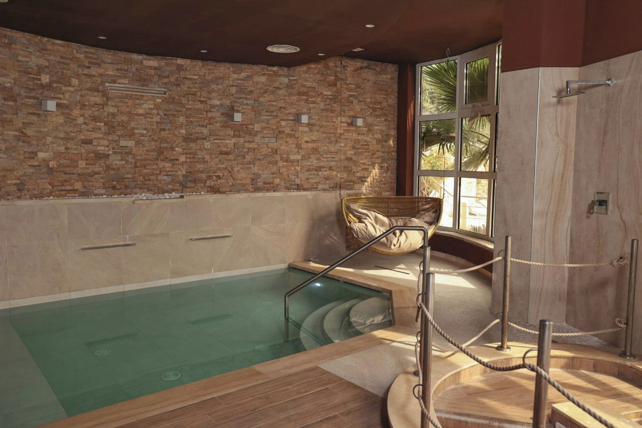 Uma área de spa com parede de pedra, deck de madeira e piscina envidraçada.