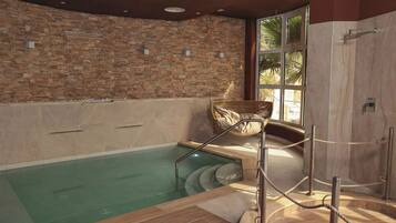 Uma área de spa com parede de pedra, deck de madeira e piscina envidraçada.