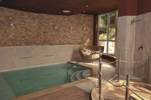 A spa area with a stone wall, a wooden deck, and a glass-enclosed pool. - Tenuta Contessa Relais Country House (Lattarico)