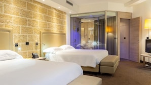 Een hotelkamer met twee bedden, een stenen muur, een douche met glazen wanden en een televisie.