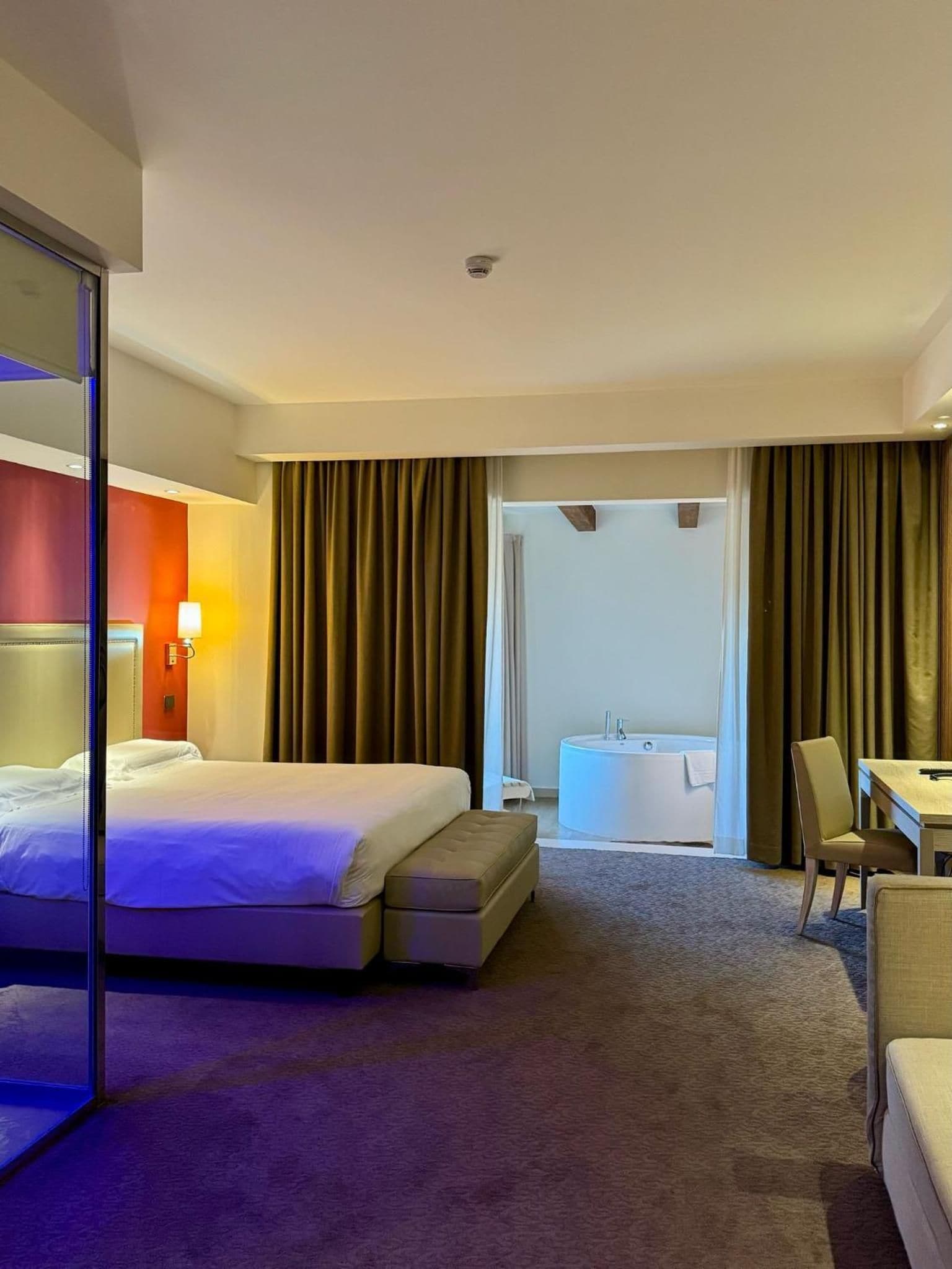 A hotel room with a bed, a desk, a chair, a bathroom with a bathtub, and a large mirror.