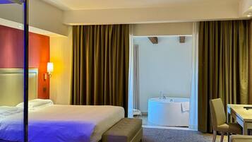 A hotel room with a bed, a desk, a chair, a bathroom with a bathtub, and a large mirror.