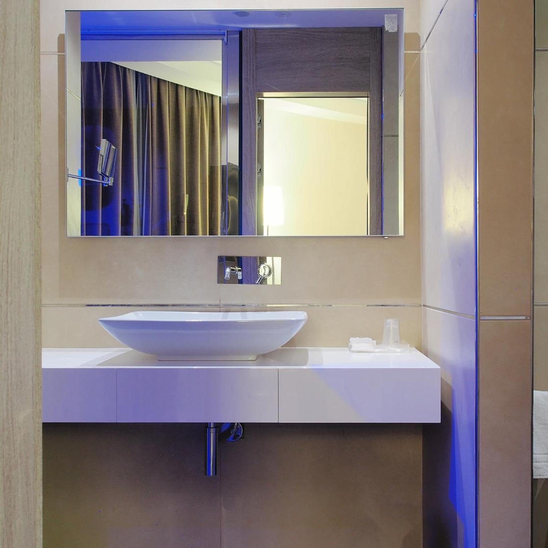A modern bathroom with a large mirror, a white sink, and a towel rack.