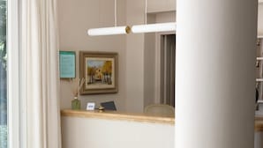 A hotel reception area with a reception desk, a framed picture on the wall, a vase with reeds, and a window with curtains. - Hotel Piccolo Mondo (Camaiore)