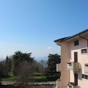 Un immeuble résidentiel doté d’un balcon, d’un panneau indiquant la présence d’un garage, et offrant une vue sur des arbres et des collines.