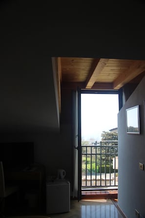 A room with a wooden ceiling, a white refrigerator, a small table with a kettle, and a view of a balcony with a gate. - Albergo Sole (San Zeno di Montagna)