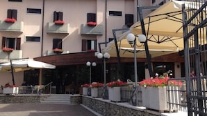 A hotel entrance with a stone facade, outdoor seating, and a covered area with umbrellas. - Albergo Sole (San Zeno di Montagna)