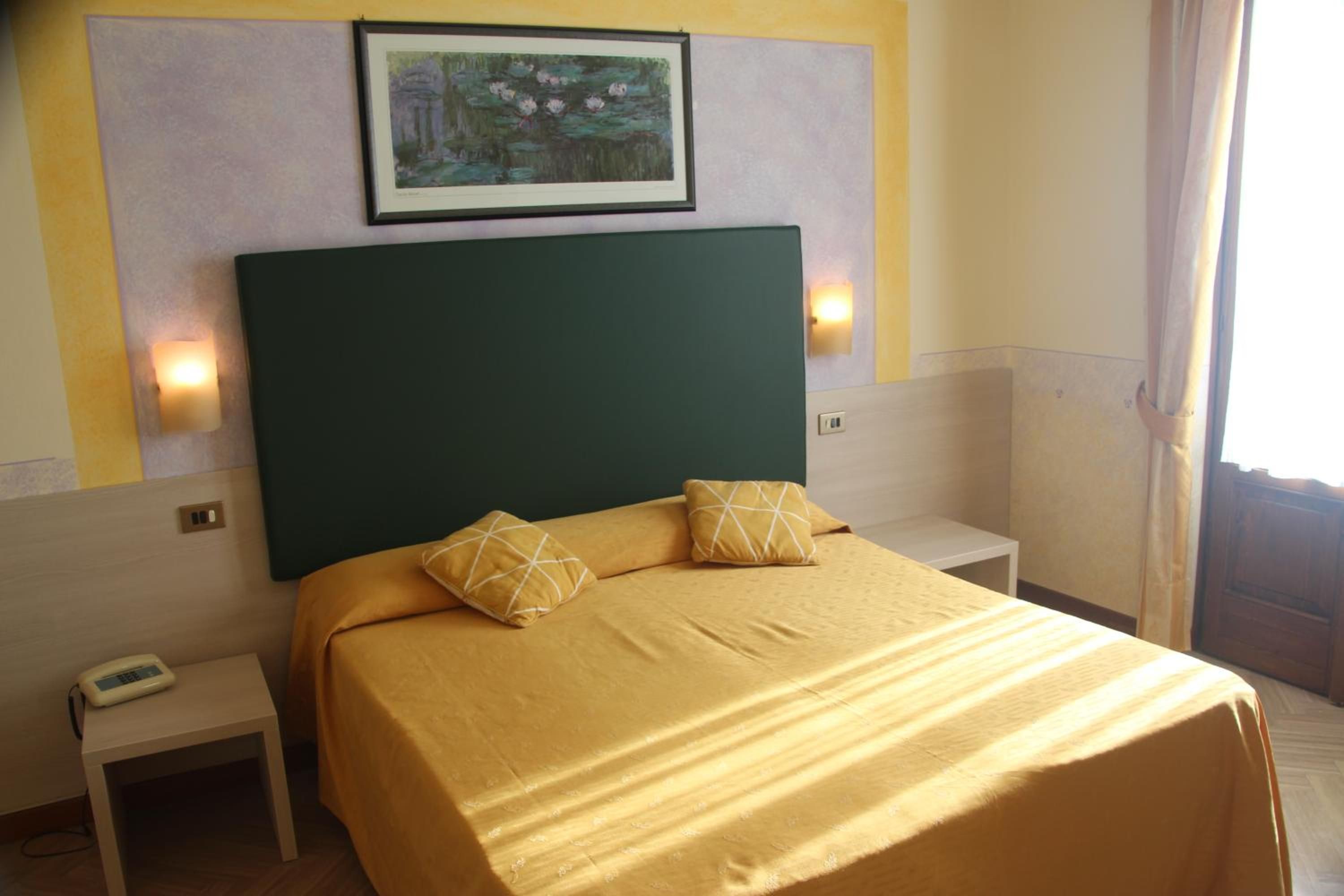 Ein Hotelzimmer mit einem Bett, zwei Nachttischen, einem Telefon und einem Bild an der Wand.