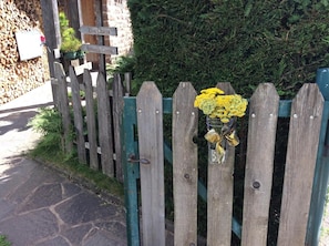A wooden fence with a metal gate, a sign with names, and a bouquet of yellow flowers. - Albergo Sole (San Zeno di Montagna)