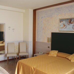 Une chambre d’hôtel avec un grand lit, deux chaises, une table de chevet et un tableau au mur.