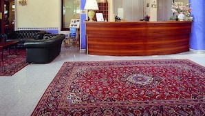 A reception area with a wooden reception desk, a patterned rug, a sofa, and a sun decoration on the wall. - Albergo Sole (San Zeno di Montagna)