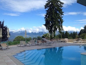 A pool area with lounge chairs and umbrellas, surrounded by trees and a mountain view. - Albergo Sole (San Zeno di Montagna)