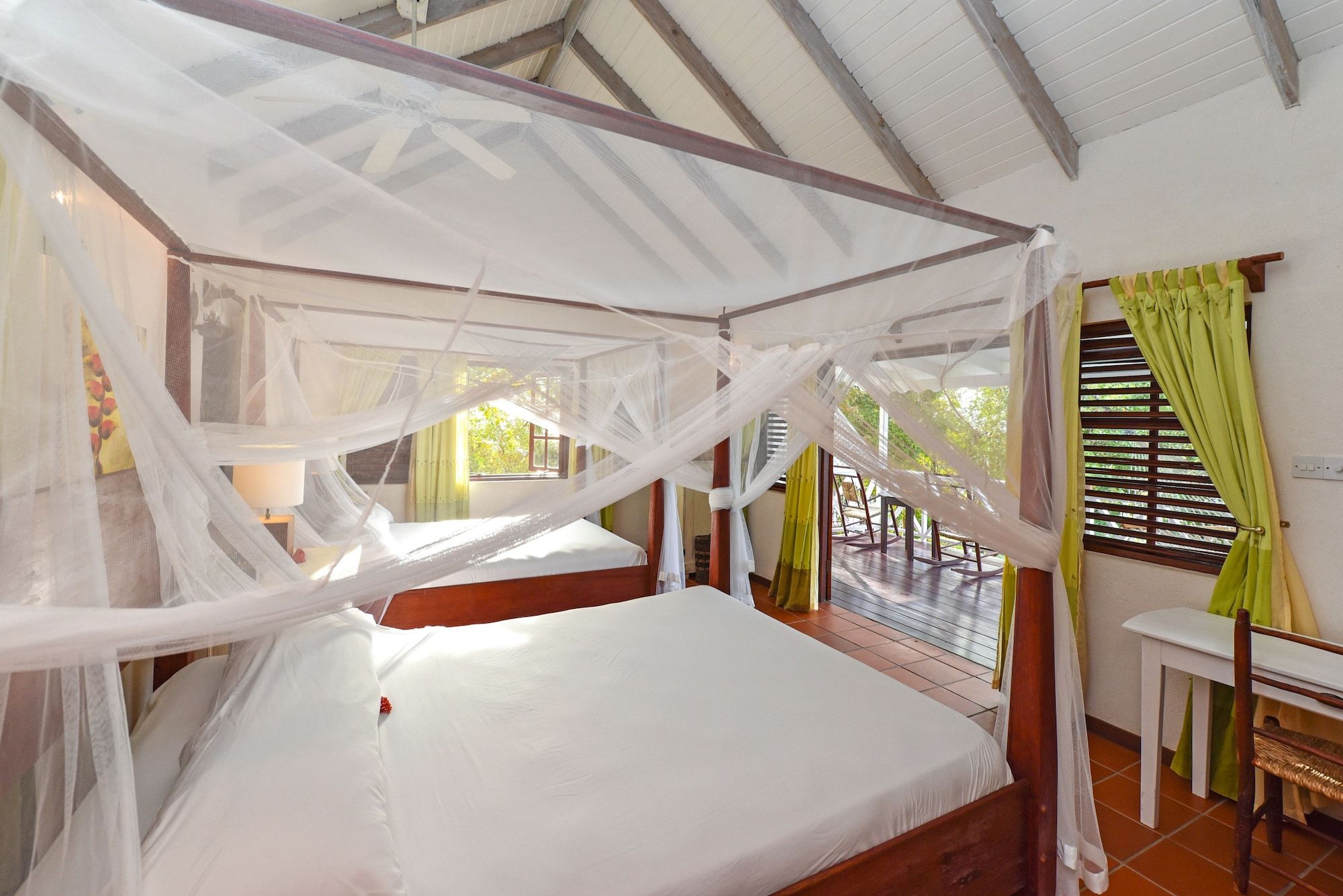 A room with a bed under a mosquito net, a window with curtains, and a view of the outdoors.