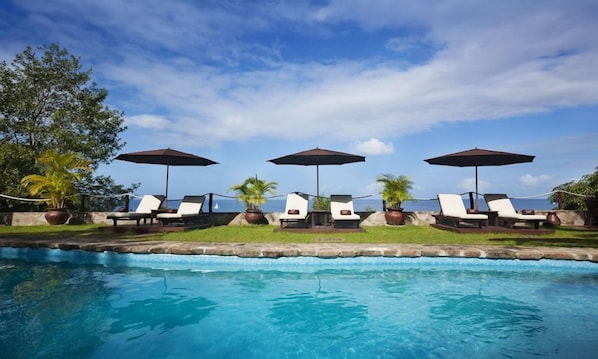 Une piscine entourée de verdure, avec des chaises longues et des parasols.