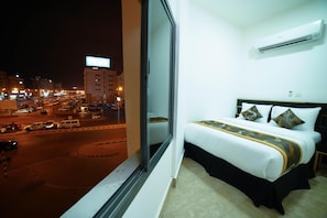 Quarto de hotel com uma grande janela com vista para uma rua movimentada à noite.
